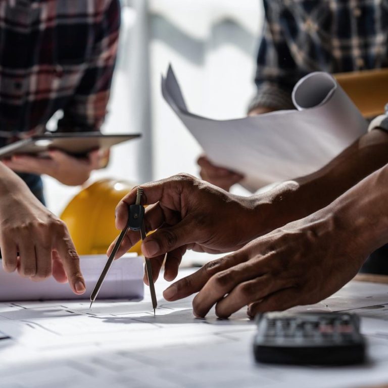 Hände, die an Bauplänen arbeiten, mit Zeichengeräten und Dokumenten.