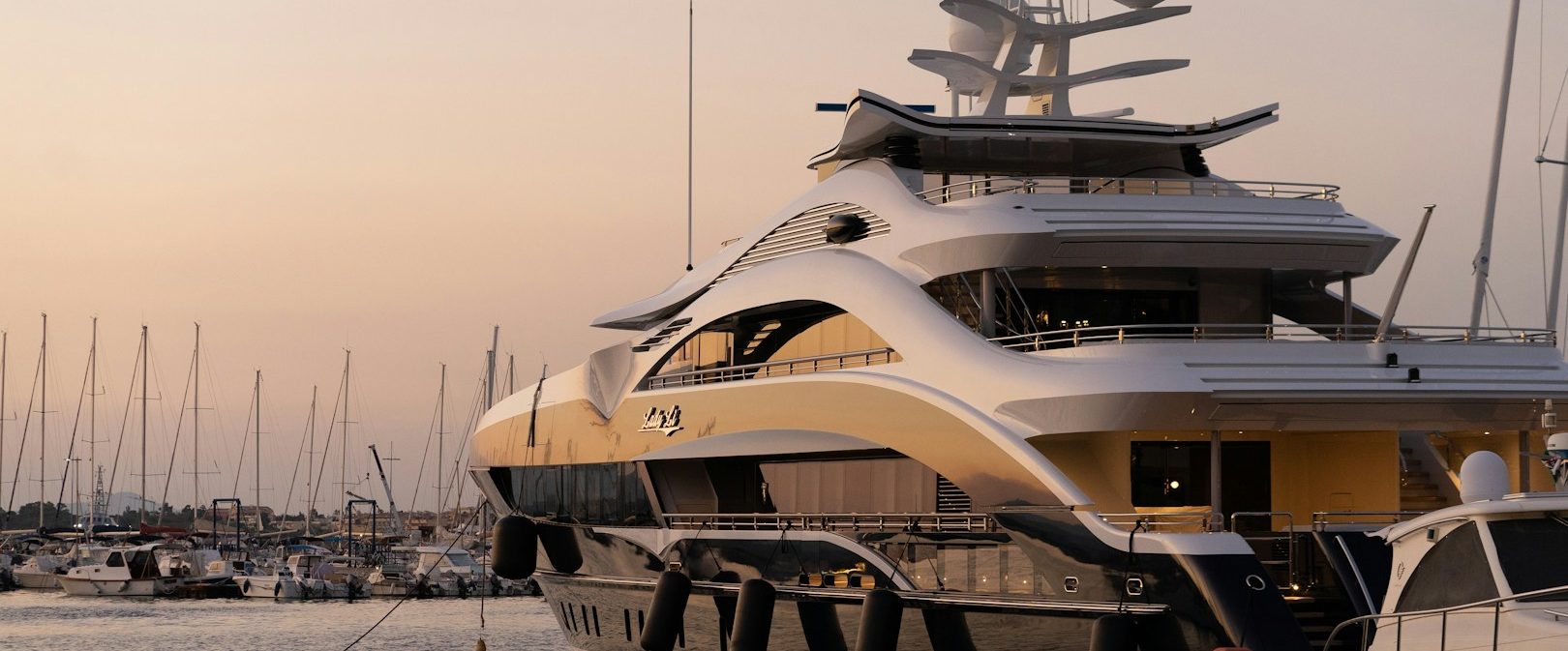 Luxusyacht am Hafen bei Sonnenuntergang, umgeben von Segelbooten.